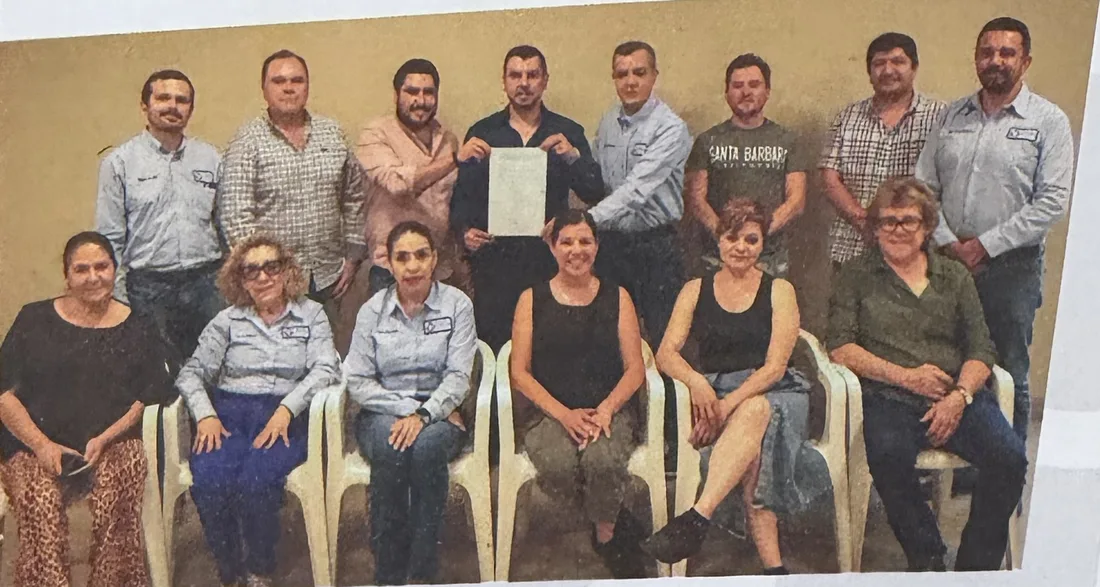 Group of about fifteen people, standing and seated, holding a signed document